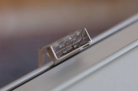 The hinge holding the clear plastic pen holder, viewed from the other side. It is now flipped down (in the position the pen is touching the paper), and the back of the spring wire is visible.