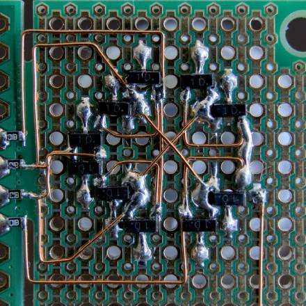 Bottom of a PCB, where ten SOT-23 transistors are soldered in a circle. Enamelled wire connected their various pins to four SMD resistors.