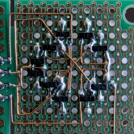 Bottom of a PCB, where ten SOT-23 transistors are soldered in a circle. Enamelled wire connected their various pins to four SMD resistors.